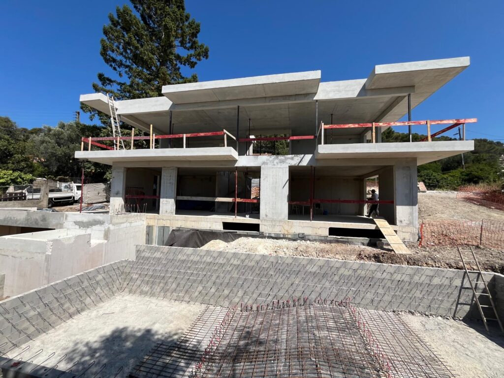 Maison Moderne Béton : Gros Œuvre et Piscine en Cours Construction d'une maison moderne en béton brut, vue sur la structure et le coffrage d'une piscine.