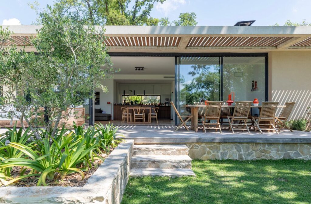 Terrasse bois moderne avec salon extérieur et jardin Maison moderne avec terrasse en bois, salon extérieur et grand olivier surplombant une pelouse verte et des marches en pierre.