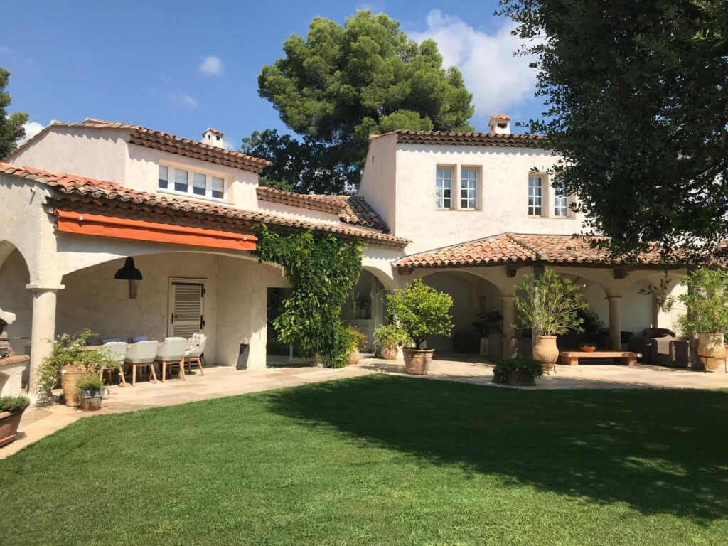 Villa Provençale de Luxe avec Jardin Méditerranéen Belle villa provençale avec toits de tuiles rouges, pelouse verte bien entretenue et terrasse couverte avec mobilier d'extérieur.