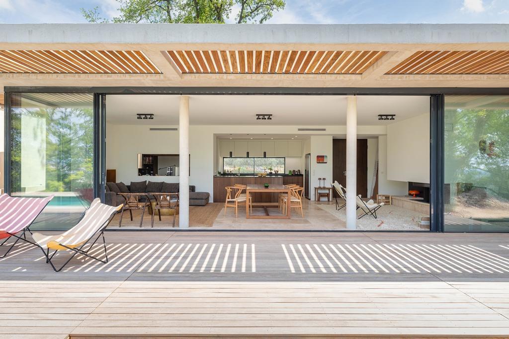 Design Maison Moderne : Terrasse Bois et Intérieur Ouvert Terrasse en bois moderne s'ouvrant sur un salon-cuisine lumineux avec mobilier contemporain et chaises longues extérieures.