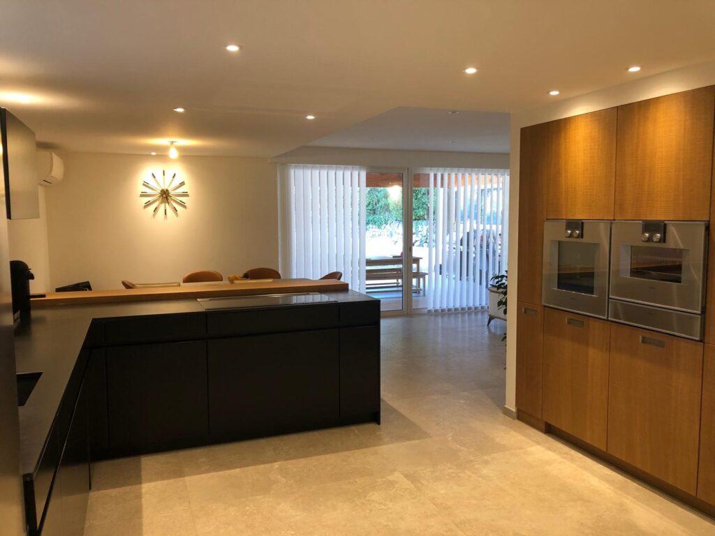 Cuisine moderne avec îlot noir, meubles en bois, fours encastrés et horloge murale design lumineuse.