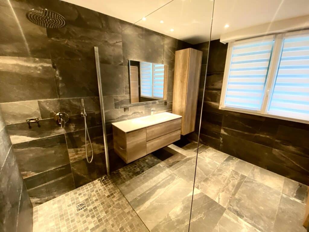 Salle de bain moderne : douche à l'italienne en pierre grise, meuble vasque bois suspendu et carrelage assorti.