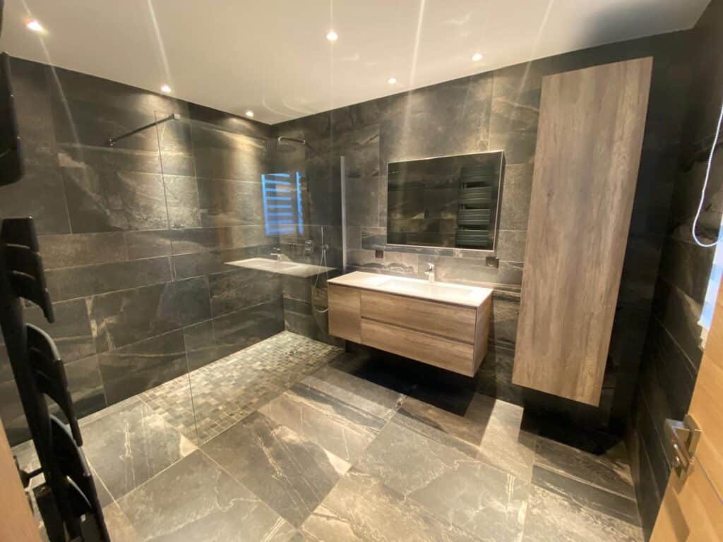Salle de bain moderne avec douche à l'italienne, carrelage pierre grise et meuble vasque en bois clair suspendu.